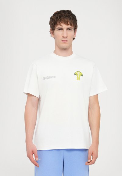 T-shirt en coton blanc avec un graphique de brocoli vert sur la poitrine et un texte imprimé sur le côté gauche. Manches courtes, coupe décontractée.