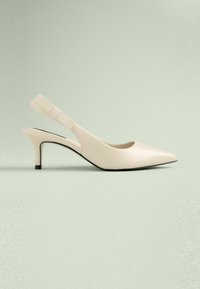 Slingback-kengät vaaleassa kiiltävässä nahassa, joissa on teräväkärkinen muoto, hoikka korkea korko ja koristeellinen nauha säädettävässä hihnassa.