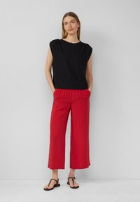 Zwart mouwloos top met een ronde hals, gecombineerd met losse, rode broek tot de enkels en zwarte slippers. Glad textuur van de stof.
