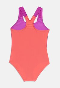 Maillot de bain dos nageur avec un devant corail et des bretelles violettes, fabriqué en tissu extensible, présentant une texture lisse et un design ajusté.