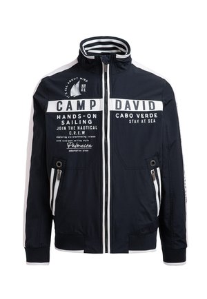 Marineblaue Jacke mit weißen Akzenten und Text; verfügt über einen hohen Kragen, Reißverschlusstaschen und gerippte Bündchen. Maritim inspirierte Designelemente vorhanden.