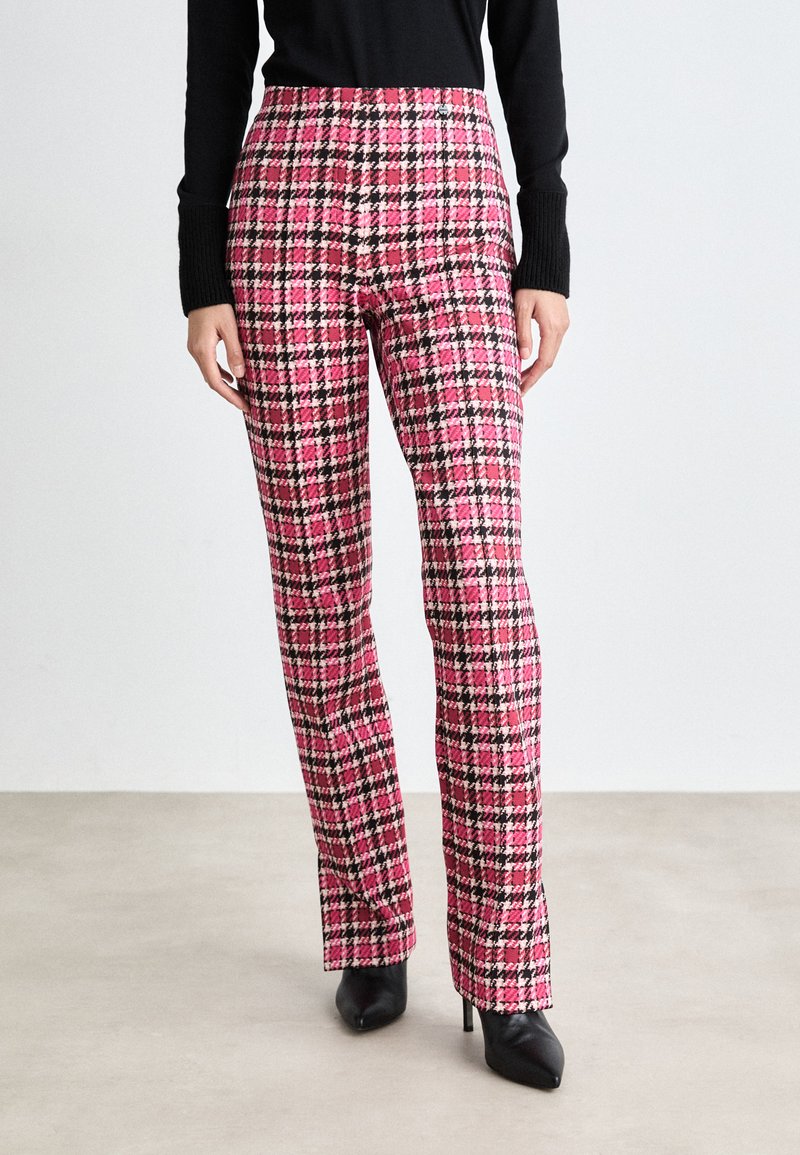 Pantalons taille haute à carreaux roses et noirs en tissu texturé avec une coupe droite, associés à des chaussures à talons noires.