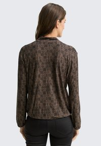 Long-sleeve blouse with a textured black and brown striped pattern, featuring a relaxed fit and a high neckline. Made of lightweight fabric.
