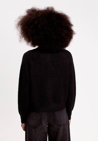 Pull en tricot noir à coupe décontractée, avec des poignets et un ourlet côtelés, et une texture douce. Associé à un pantalon en denim gris taille haute.