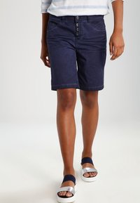 Navyblauwe katoenen shorts met een knoopsluiting en vijf zakken. Het ontwerp heeft een rechte snit en omgeslagen zoom, in combinatie met platform sandalen.