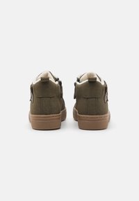 Bottes montantes en daim vert avec doublure en polaire beige, semelles en caoutchouc marron et détails cousus. Présente un bout arrondi et une languette à l'arrière.
