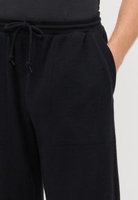 Schwarze Hosen aus strukturiertem Stoff, mit einem elastischen Bund und Kordelzug sowie zwei Vordertaschen.