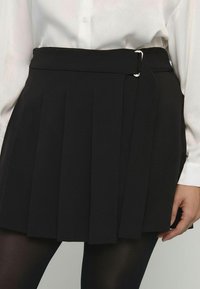 Schwarzer Faltenrock mit einem breiten Bund und einem silbernen Schnallendetail. Hergestellt aus glattem Stoff, mit einem klaren, strukturierten Design.