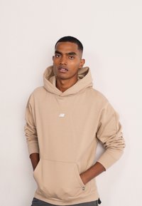 Felpa beige realizzata in materiale morbido, con tasca frontale e un piccolo logo sul petto. Maniche lunghe con polsini.