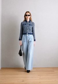 Veste courte tissée bleu marine et blanche avec poches, assortie à un jean large bleu clair. Accessoirisée avec des lunettes de soleil sombres et un petit sac noir.