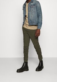 Jeansjacka med en ljusblå tvätt, ribbade ärmslut och bröstfickor; beige tröja med rund hals; olivgröna tapered-byxor; svarta ankelboots.