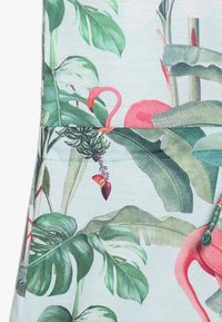 Tyg med tropiskt mönster som har gröna bananblad, monstera blad och rosa flamingos på en ljus bakgrund.