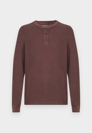 Dug garašni tamnosmeđi henley majica s dugim rukavima i rebrastom teksturom, s tri gumba na prednjem dijelu i okruglim izrezom.