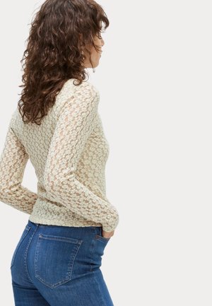 Top in pizzo crema con maniche lunghe, dalla silhouette aderente e motivo floreale testurizzato, abbinato a jeans in denim blu con tasche standard.