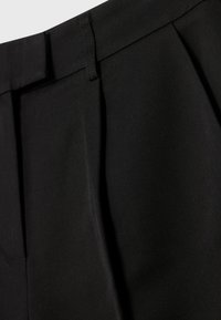 Pantalones negros plisados con una tela suave y texturizada. El diseño incluye una cinturilla con trabillas y líneas limpias.