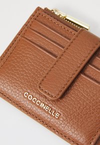 Brown leather wallet with a textured surface, featuring multiple card slots, a zip pocket, and gold-tone hardware detailing.