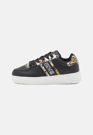 Czarny niski sneaker z białą podeszwą, czarnymi sznurówkami, złotymi i białymi wzorzystymi akcentami oraz logo Versace Jeans Couture po boku.