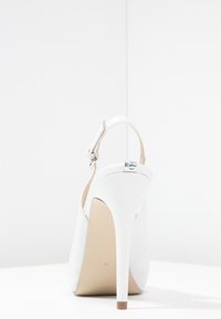 Scarpa bianca con tacco alto e design slingback, in morbida pelle, punta affusolata e sottile tacco a stiletto. Accento argentato sul tacco.