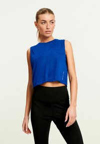 Blå ærmeløs cropped top med tekstureret b�ølgemønster og subtilt mærkedetalje, parret med højtaljede sorte leggings.