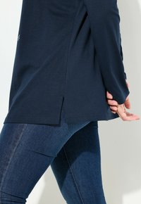 Top a maniche lunghe blu navy in morbido tessuto, dotato di fessure laterali, abbinato a jeans slim in denim scuro che mettono in risalto un look casual.