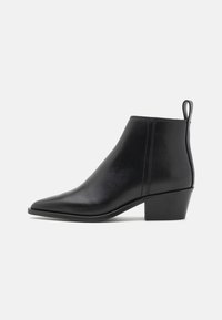 Botas de couro pretas até ao tornozelo, com bico pontudo, ligeiro salto e alça na parte de trás para facilitar o calçar. Textura suave e detalhes cosidos nas laterais.
