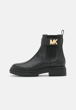 Botte noire en cuir à la cheville avec semelle épaisse, panneau latéral élastique, languette de traction et logo MK doré sur la sangle près du haut.