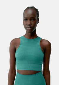 Een aangesloten, mouwloze crop top in een effen teal kleur, met ribbelstructuur en een uitsnijding in de taille.