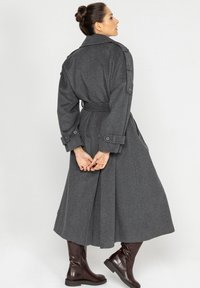 Szary wełniany trench coat z paskiem w talii, naramiennikami i długimi rękawami, noszony na brązowe skórzane botki do kolan.