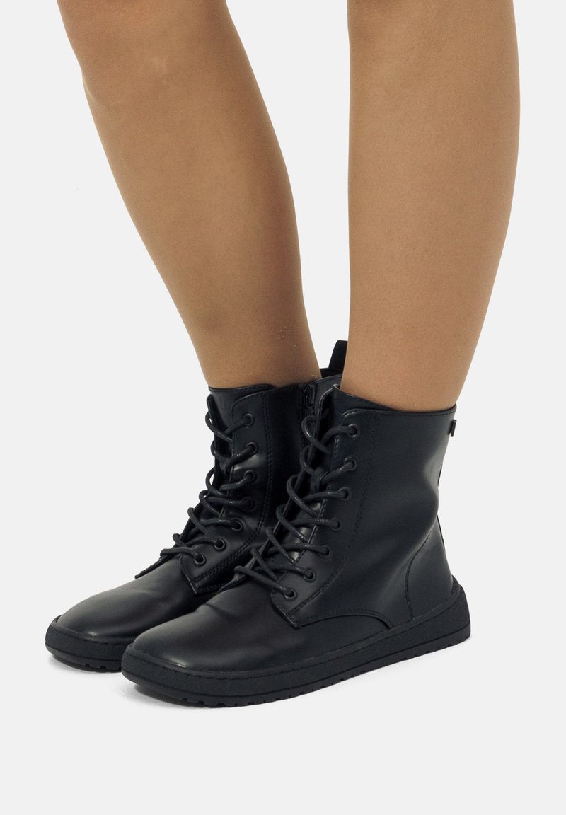 Botas de tobillo de cuero negro con cordones en la parte delantera, puntera redonda, suela de goma texturizada y detalle sutil del logo en el lateral. Acabado suave.