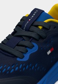 Αθλητικό παπούτσι σε ναυτικό μπλε με υφασμάτινο επάνω μέρος με υφή, γκρι κορδόνια, κίτρινα στοιχεία και μπλε σόλα. Διαθέτει ταμπέλα με λογότυπο και διάτρητο σχέδιο.