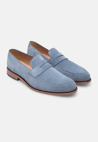 Helles blaues Wildleder-Loafer mit einem gestickten Design, ausgestattet mit einem erhöhten Riemen und braunen Ledersohlen. Glatte Textur und klassisches Shape.