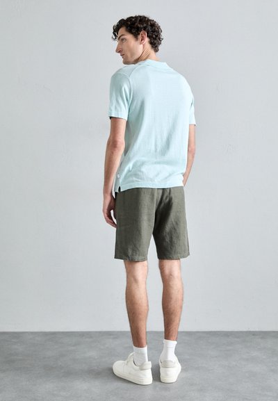 Chemise à manches courtes bleu clair, short vert et baskets blanches. Le tissu semble doux, avec une coupe décontractée et des fentes sur les côtés de l'ourlet de la chemise.