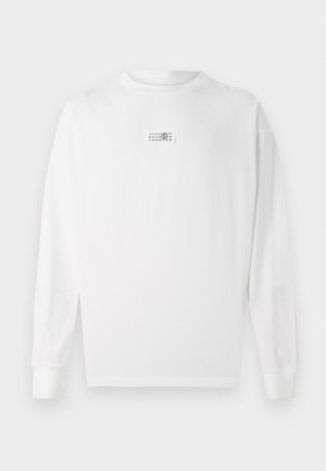 T-shirt blanc à manches longues en coton, avec une petite étiquette graphique sur la poitrine et des poignets côtelés. Design simple et coupe droite.