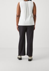 Bílý bezrukávový top s texturovaným zadním dílem, kombinovaný s volnými černými kalhotami s vzorem. Jednoduchý design s měkkou tkaninou a neutrálními barvami.