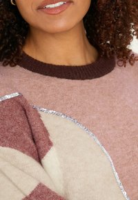 Sweter dzianinowy w odcieniach różu z brązowym ściągaczem, z kremowym panelem, ozdobiony srebrnymi cekinami wzdłuż krawędzi.