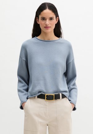 Light blue knitted sweater with a wide neckline and relaxed fit, paired with beige trousers and a black belt featuring a gold buckle.