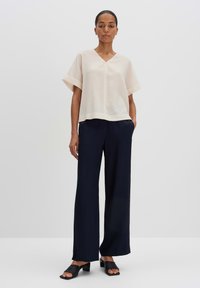 Top corto a maniche corte di un beige chiaro con scollatura a V e vestibilità rilassata, abbinato a pantaloni a gamba larga blu navy scuro e décolleté neri senza lacci.