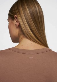 T-shirt in cotone marrone con scollatura girocollo; il dettaglio di cucitura sul retro presenta due linee parallele. Morbida texture e vestibilità casual.