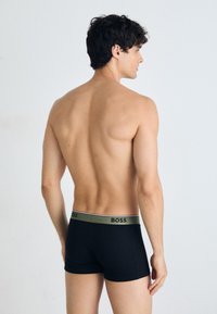 Schwarze Boxershorts aus weichem Stoff, mit einem grünen Bund, auf dem das "BOSS"-Logo prangt. Modell von hinten gezeigt, ohne Oberteil.
