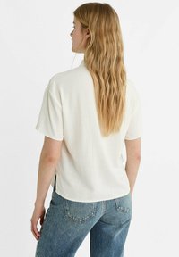 Top bianco a maniche corte con una vestibilità comoda, caratterizzato da una sottile texture e spacco laterale, abbinato a jeans a vita alta blu.