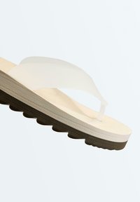 Sandale tongs blanche avec des larges brides transparentes et une semelle intérieure beige matelassée, dotée d'une semelle noire texturée antidérapante.