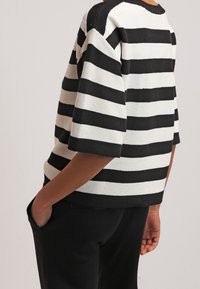 Czarnobiały prążkowany dzianinowy top z krótkimi rękawami, o luźnym kroju i fakturowanej powierzchni. Wzór naprzemiennie przedstawia szerokie paski.