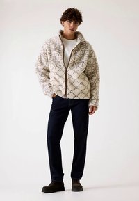 Off-White flauschige Zip-up-Jacke mit einem geometrischen Muster, langen Ärmeln und einem hohen Kragen, kombiniert mit dunkelblauen Jeans und Schuhen.