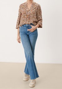 Brun blomstret bluse med v-hals og klokkeærmer, parret med lyseblå flare jeans og beige chunky sneakers.