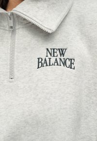 Γκρι φούτερ με γιακά και φερμουάρ μέχρι τη μέση, με κεντημένο λογότυπο «New Balance» σε σκουρό γκρι στο στήθος. Μαλακή υφή.
