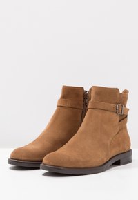 Bruna mocka ankelskor med dragkedja på sidan, ett band med ett metallspänne, rund tå och en låg svart klack.