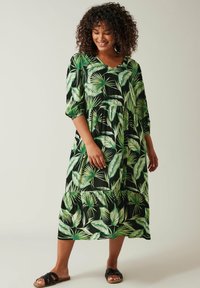 Zwarte jurk met groen loofpatroon, V-hals, 3/4 mouwen, gerimpelde taille en gelaagde rok. Zachte stof en comfortabele pasvorm. Zwarte sandalen.