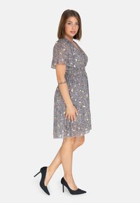 Kurzes navyblaues Kleid mit floralem Muster; weicher, leichter Stoff; kurze, flatternde Ärmel; ausgestellt Rock; Model trägt schwarze High Heels.