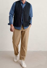 Schwarzes Baumwollhemd über einem blau gestreiften Shirt, kombiniert mit beigen Hosen. Weiße Sneaker vervollständigen das Outfit. Einfaches Design und lässige Passform.