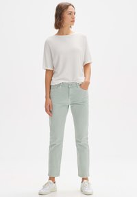 Top corto a maniche corte grigio chiaro con texture abbinato a jeans slim fit verde menta e sneakers bianche. I jeans presentano una chiusura con bottone e tasche.